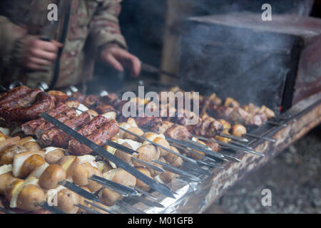 The cook prepares meat on the skewer and tests the readiness of the meat with a large knife. Stock Photo