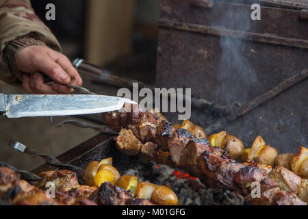 The cook prepares meat on the skewer and tests the readiness of the meat with a large knife. Stock Photo