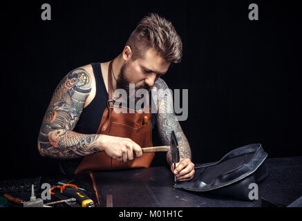 Artist working with leather works with leather goods./Leather workman producing a leatherwork at his workshop. Stock Photo