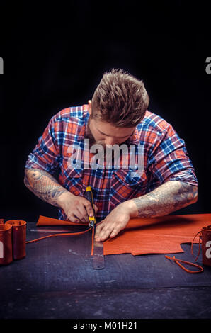 Leather man demostrating leather cutting process at studio./Currier of leather cuts out leather goods at leather studio. Stock Photo