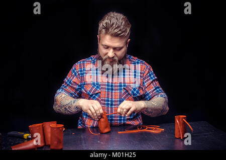 Man working with leather producing leather workpiece in his tanning shop./Leather workman processes a workpiece from leather. Stock Photo
