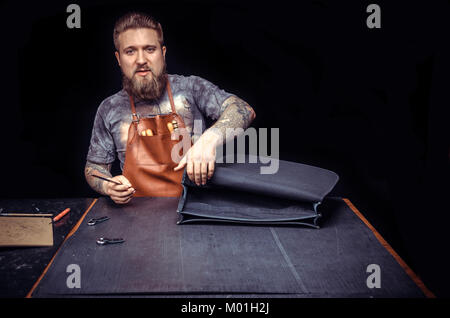 Worker of leather producing leather workpiece./Leather Currier performs leather working for a new product at his studio. Stock Photo