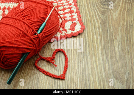 crochet red heart with wool ball and oven cloth with copy space on wooden table background Stock Photo