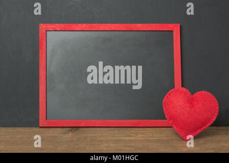 Chalkboard frame with place for your text and red felt heart as decor on wooden table. Valentine's card. Template. Stock Photo