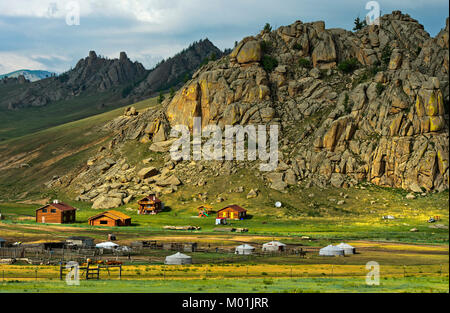 Hamlet with yurts and blockhouses in front of a rocky peak in the Mongolian steppe, Gorkhi-Terelj National Park, Mongolia Stock Photo