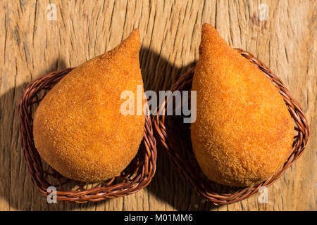 Deep fried chicken finger food known as Coxinha in Brazil. Brazilians eat as fast food alternative or at parties. Two snacks in basket on rustic wood, Stock Photo