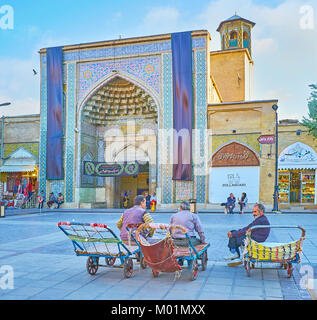 SHIRAZ, IRAN - OCTOBER 12, 2017: Three porters rest and talk, sitting on their empty carts, at the main entrance to Vakil mosque with beautiful tiled  Stock Photo