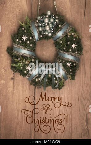 Decorated Christmas wreath on wooden door, text 'Merry Christmas'. Stock Photo