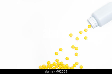 Yellow film coated tablets pills spilling out of pill bottle on white background with copy space. Painkiller tablet pills. NSAIDs pills for muscle pai Stock Photo