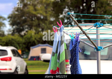 St Leonards, Hampshire, UK - May 30th 2017: Towel and swimsuit hanging on a rotary camping clothes drier on a campsite, with car, tent and caravan in  Stock Photo