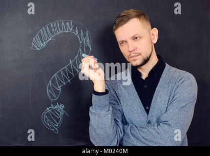a bearded man thinks near a black school board with question mark on it Stock Photo