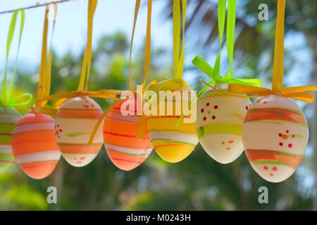 Easter decoration, colourful Easter eggs hanging on a rope in a tropical backyard. Stock Photo