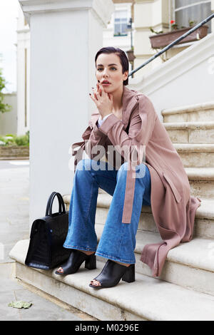 Woman in coat and jeans sitting on steps outside a house Stock Photo