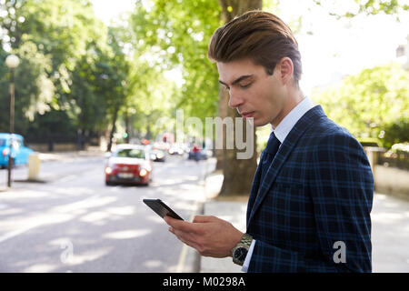 Young businessman standing in the street using smartphone Stock Photo