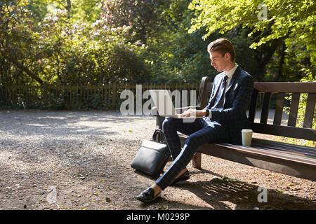 Young businessman using laptop on park bench Stock Photo