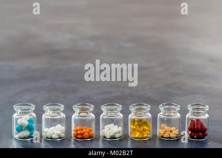 Medicine Concept: line of Medicine Tablets in opened glass Bottle with multi colored plastic caps on slate background Stock Photo