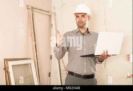 Adult man architect managing process with laptop in helmet indoors Stock Photo