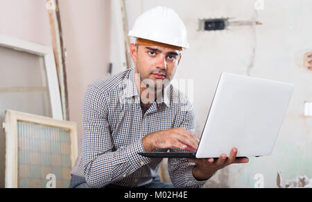 Portrait of master working at the notebook in shirt and helmet Stock Photo