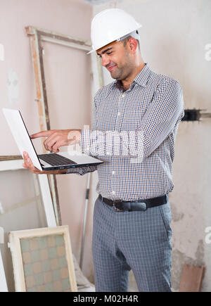 Cheerful  engineer working at the notebook in shirt and helmet Stock Photo
