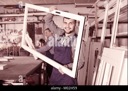 Production smiling european workers in coverall with different    finished PVC profiles and windows at factory Stock Photo