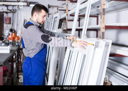 Positive adult production worker in coverall with different PVC windows and doors Stock Photo