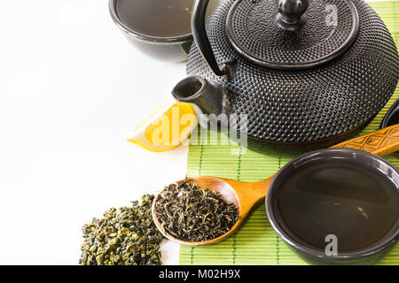 Asian green tea set on bamboo mat with dried green tea in spoon with copy space. Asian tea concept. Stock Photo