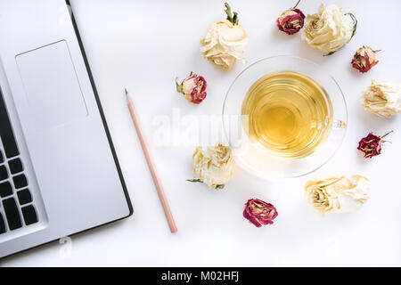 Workspace on table of pen, laptop and cup of green tea with dry roses on work table. Top view. Stock Photo