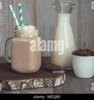 Chocolate coffee milkshake with whipped cream served in glass mason jar on gray wooden background. Summer sweet drink. Square image. Stock Photo