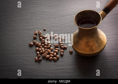 Black coffee in old copper cezve and coffee beans on black slate as background with copy space. Stock Photo