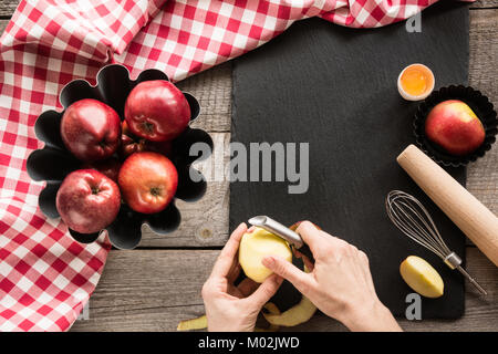 Ripe red apples on wooden board with red checkered towel around and accessories for baking. Top view. Stock Photo