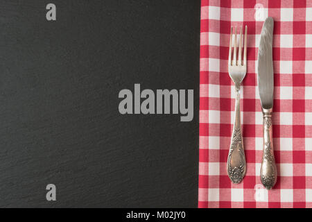Silverware with red checkered towel and empty tag on blackc slate background. Top view. Menu card for restaurants. Stock Photo