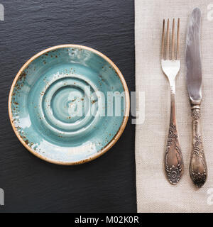 Rustic napkin, spoon and blue plate on black slate. Stock Photo