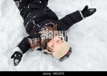 Top view of a little child dressed in warm clothes with his arms stretched wide in the snow. Boy making a snow angel.