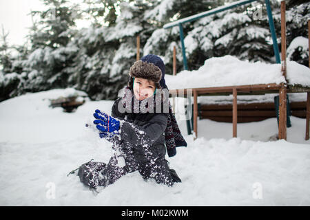 Laughing child in warm clothes having fun in a garden covered in snow. Boy enjoying snow. Stock Photo