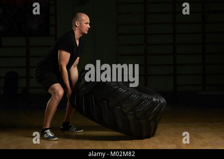 Young man lifting tire on gym background. Man working out with huge car tire Stock Photo