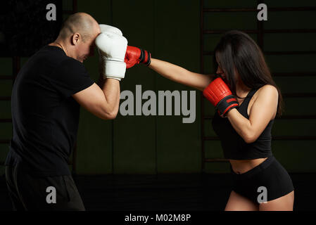 Woman kicking man in boxing fight on gym background. Personal trainer concept Stock Photo