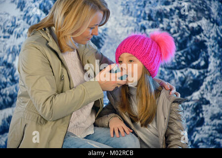 Girl using inhaler for asthma from his mothers hand in winter time Stock Photo