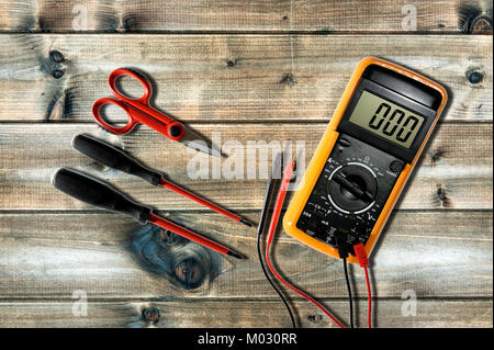 Multimeter, scissors and screwdrivers for working on a residential electrical system photographed on an antique wooden desk. Stock Photo