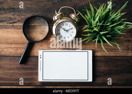 magnifying glass, clock, green plant and digital tablet with blank screen on wooden table background. digital learning concept Stock Photo