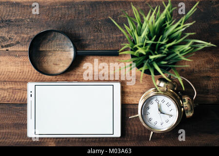 magnifying glass, clock, green plant and digital tablet with blank screen on wooden table background. digital learning concept Stock Photo