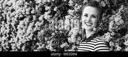 Colorful Freshness. Portrait of relaxed young woman in  stripy shirt in the front of colorful magenta flowers bed Stock Photo
