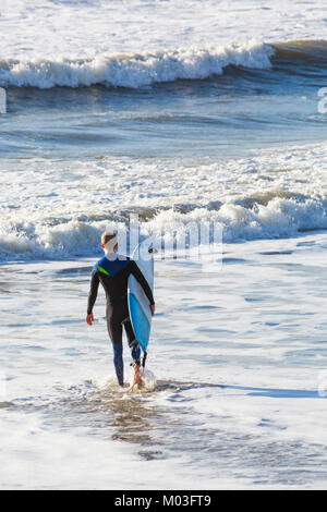 Surfer holding surf board heads into the sea to make the most of the large waves and choppy seas at Bournemouth beach Bournemouth Dorset UK in January Stock Photo