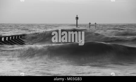 Beautiful moody black and white stormy landscape image of waves crashing onto beach at sunrise Stock Photo