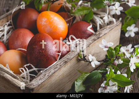 Blooming plum twigs and painted Easter eggs in rustic crate, springtime composition on wooden rural table Stock Photo