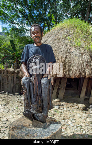 Old man in front of a traditional house showing off a mummy of a village elder Mummy presented by a member of the Dali tribe, near Wamena town in Bali Stock Photo