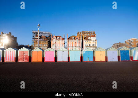 Brighton seafront 13 multi coloured beach huts, on Brighton beach promenade behind is blue sky and 3 victorian buildings, one of the buildings has sca Stock Photo