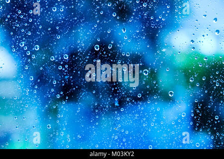 Hundreds of white rain drops on a glass window with a blurred background of blue, green, and white colours of varying shades Stock Photo