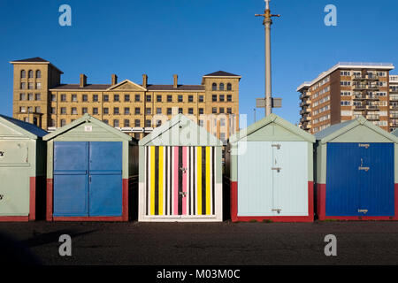 Brighton seafront five beach huts, four with blue and green doors the fifth one in the middle has a multi coloured door of yellow, pink, black stripes Stock Photo