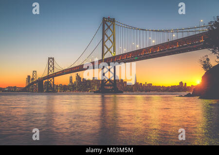 Classic panoramic view of San Francisco skyline with famous Oakland Bay Bridge illuminated in beautiful golden evening light at sunset in summer Stock Photo