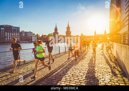 Group of female and male young runners jogging outside in golden evening light at sunset in summer with retro vintage Instagram style filter Stock Photo